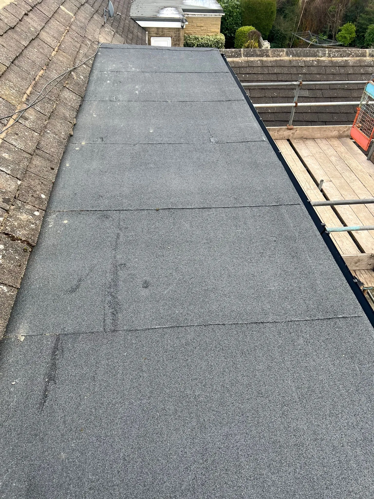 Detailed view of flat roofing felt installation next to tiled roof in Sheffield or Peak District.