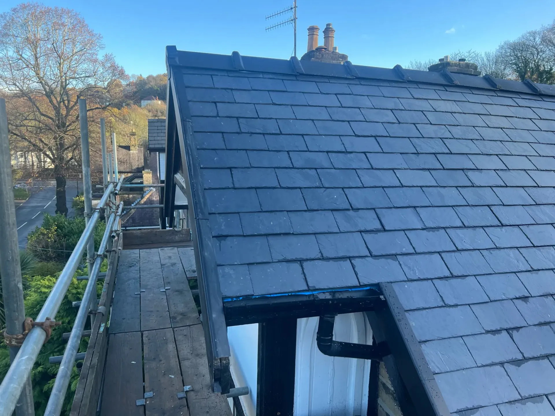 A picture of a new dark grey tiled pitched roof installation with scaffolding.