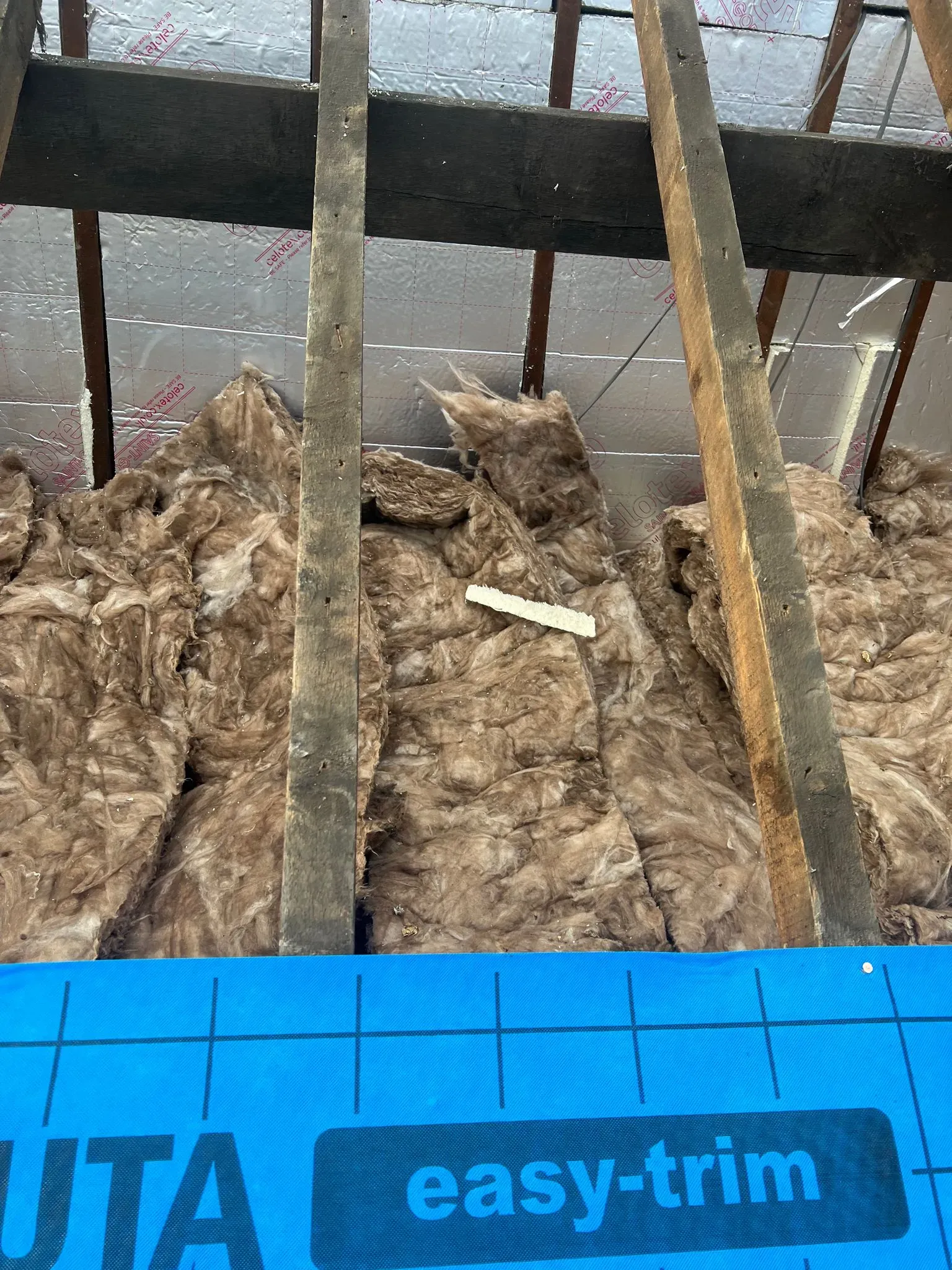 Interior view of a roof space with insulation, timber beams, and underlayment.