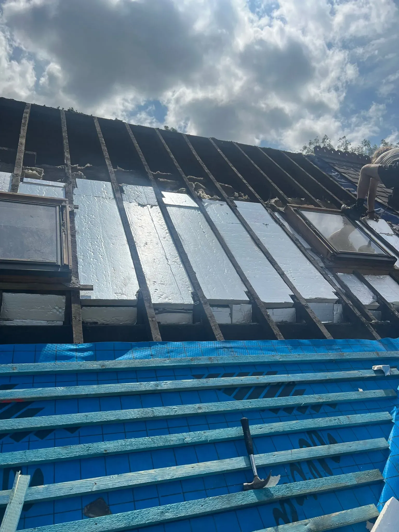 Pitched roof installation showing rafters, insulation, membrane, and battens with roof windows