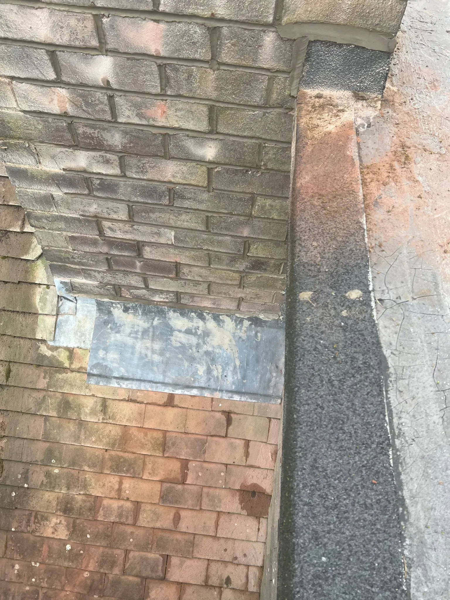 Close-up of lead flashing detail on a roof, showing tiles, brickwork, and flat roofing.