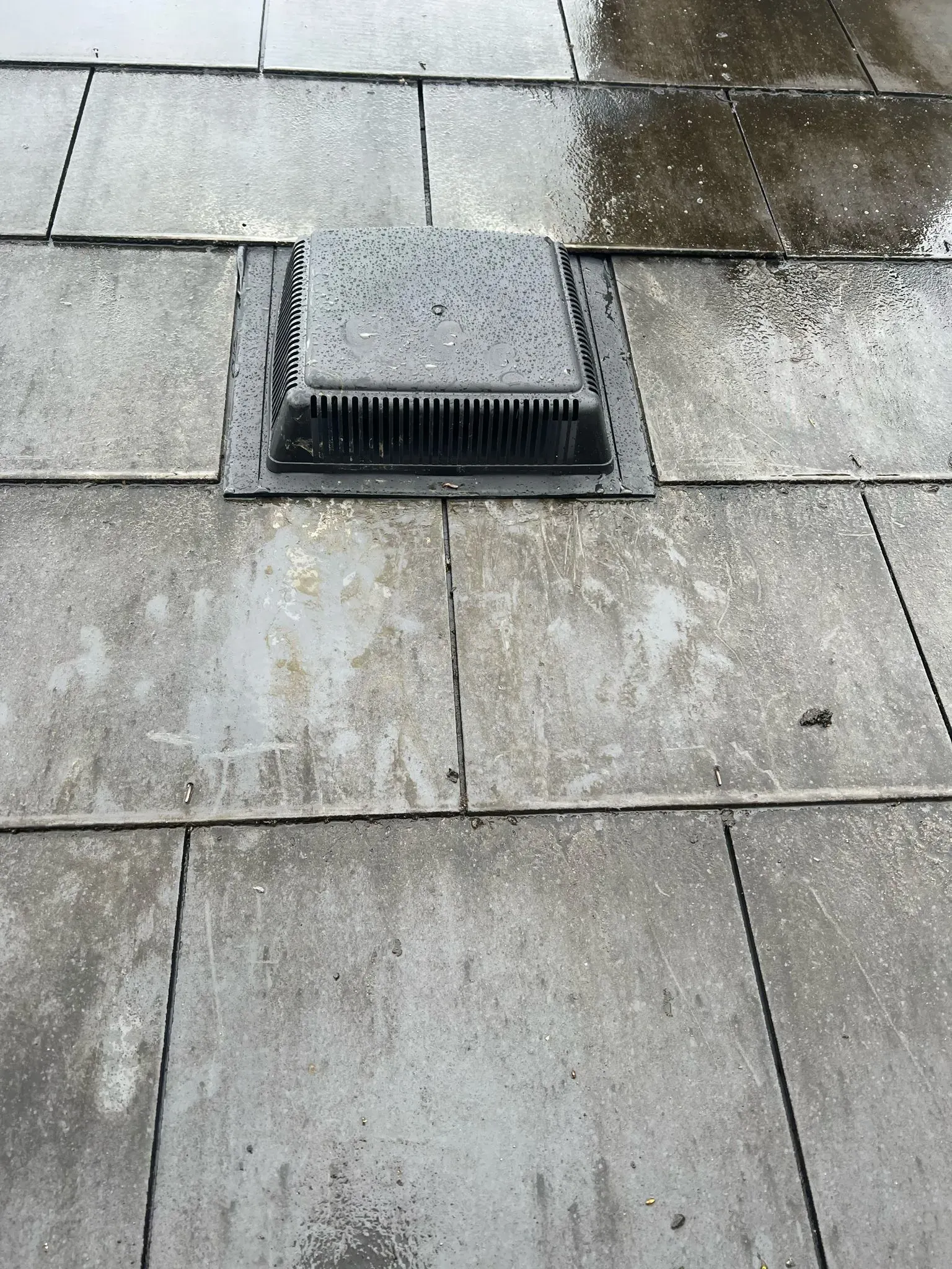 A picture of a black roof vent on grey roof tiles, showing roof ventilation.