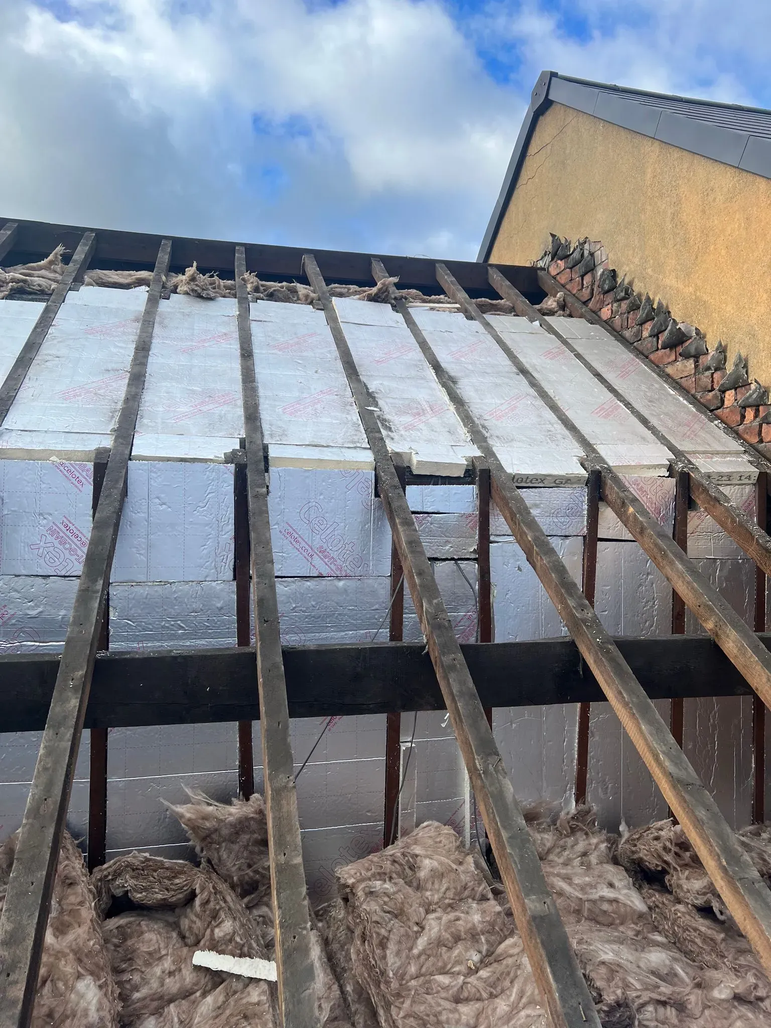 Pitched roof structure showing insulation boards and wool installed between rafters.