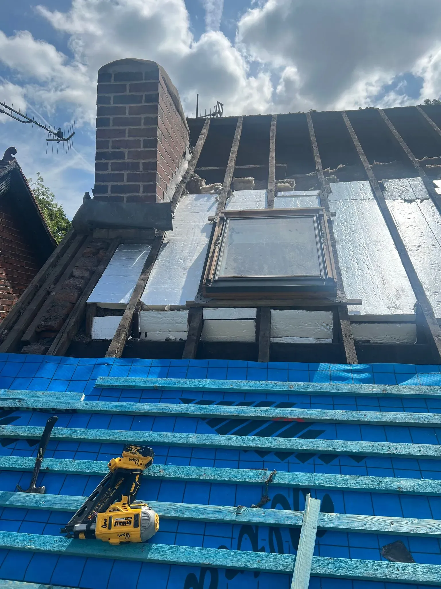 Pitched roof renovation showing new insulation, underlay, battens, chimney, and roof window installation.