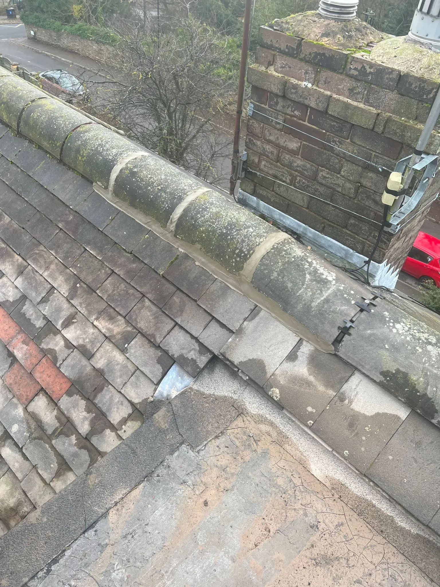 Pitched roof tiles, ridge tiles, and chimney showing signs of moss growth and wear in Sheffield or Peak District