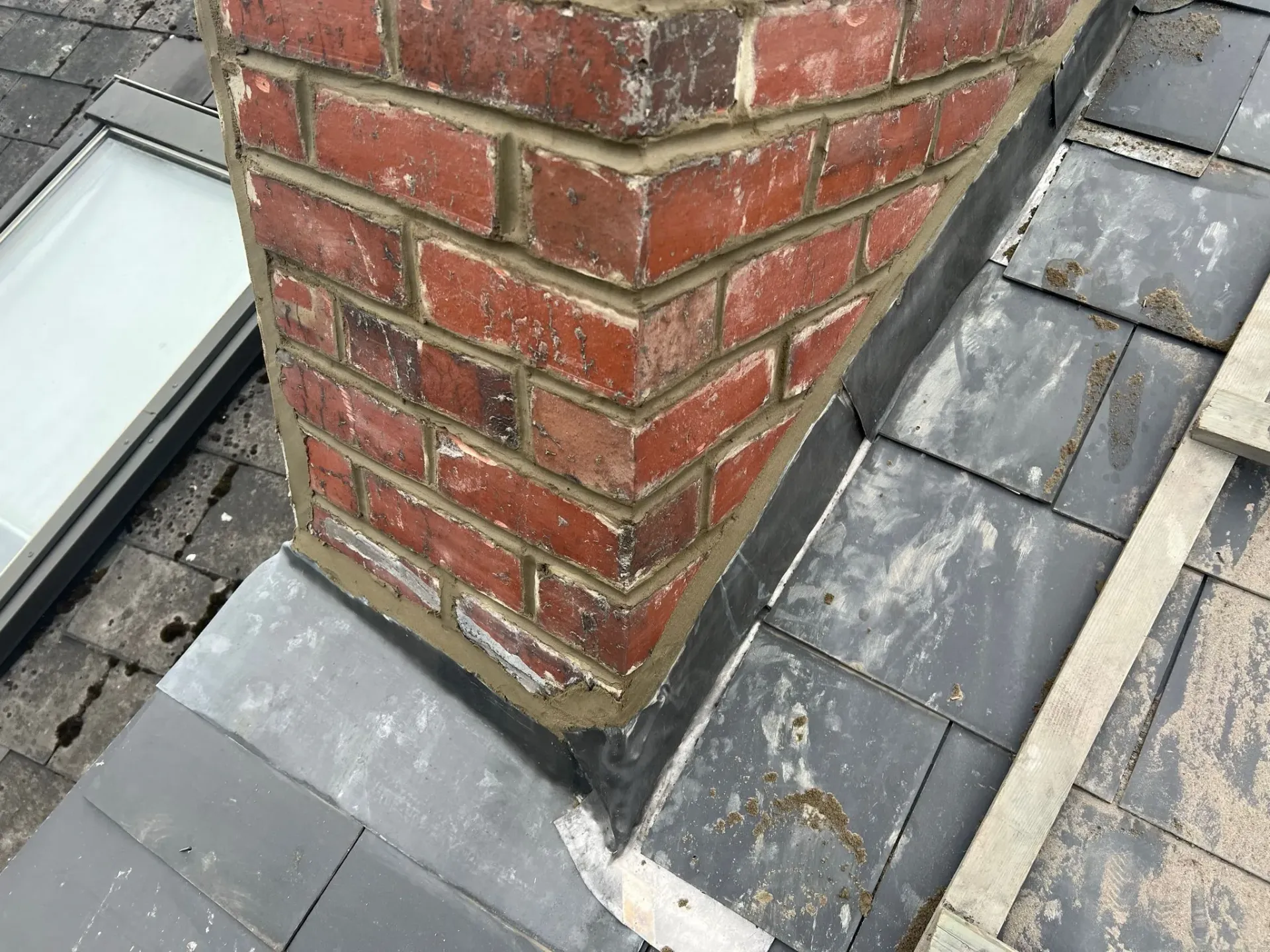Close-up of lead flashing around a chimney on a tiled roof in Sheffield, with a roof window nearby.
