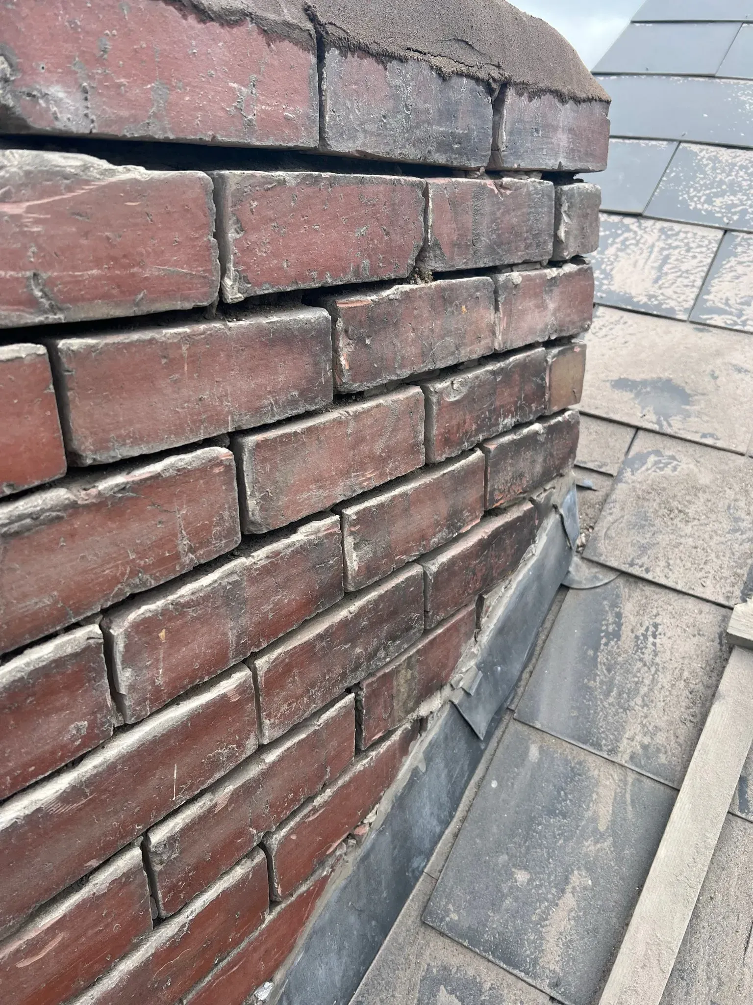 Brick chimney base with lead flashing and slate roof tiles