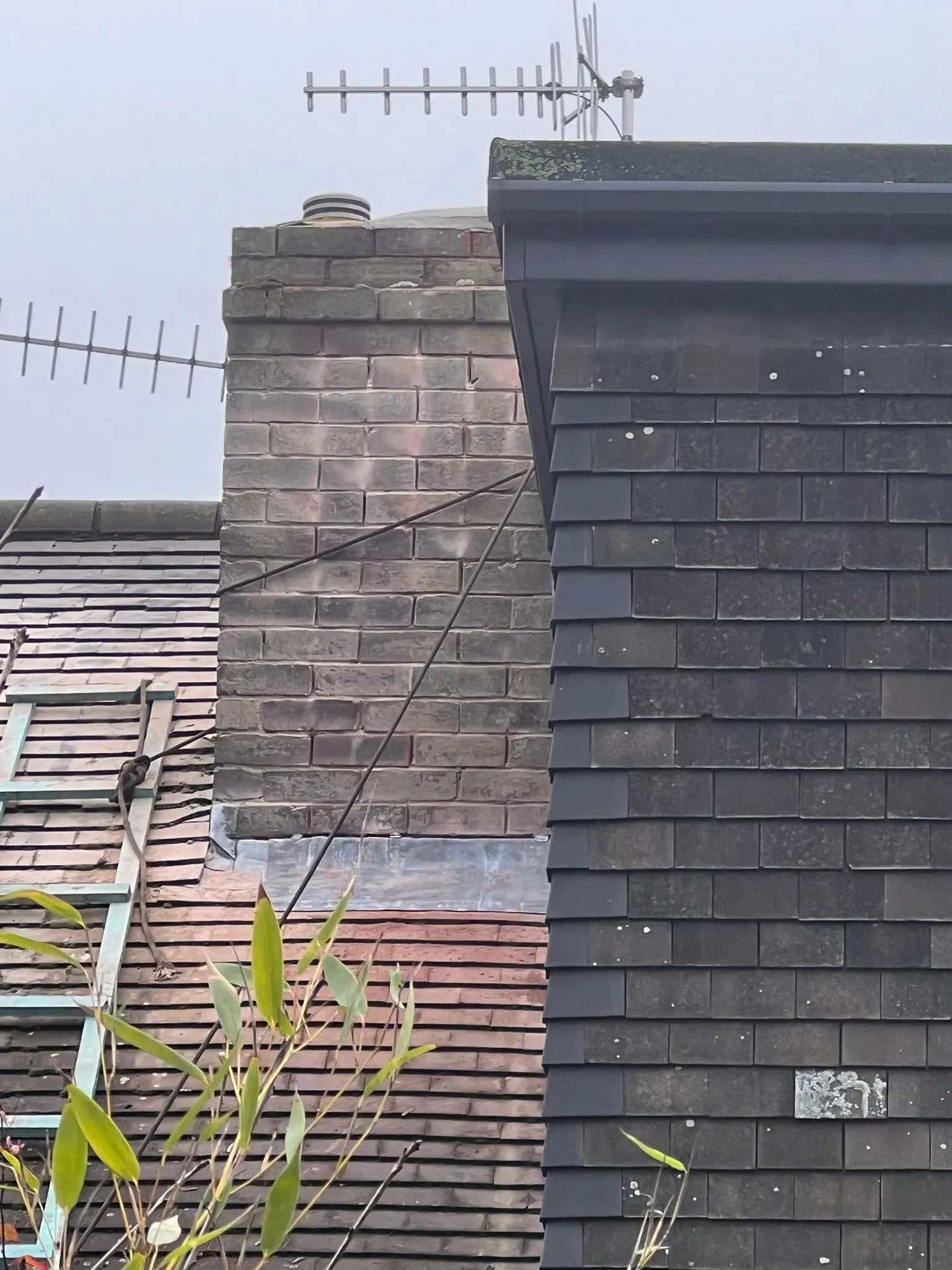 Brick chimney stack with lead flashing between tiled and slate pitched roofs