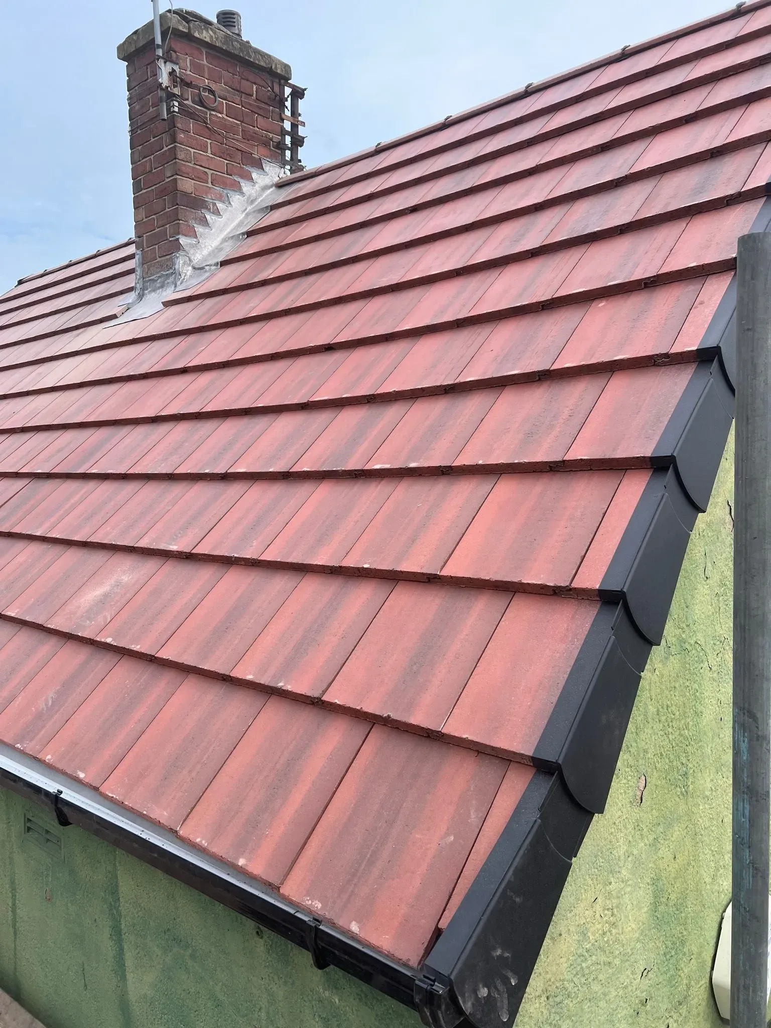 Expertly installed pitched roof with red tiles, lead flashing around a chimney, and new black uPVC fascias, soffits, and guttering in Sheffield or the Peak District by Alliance Roofing Services.
