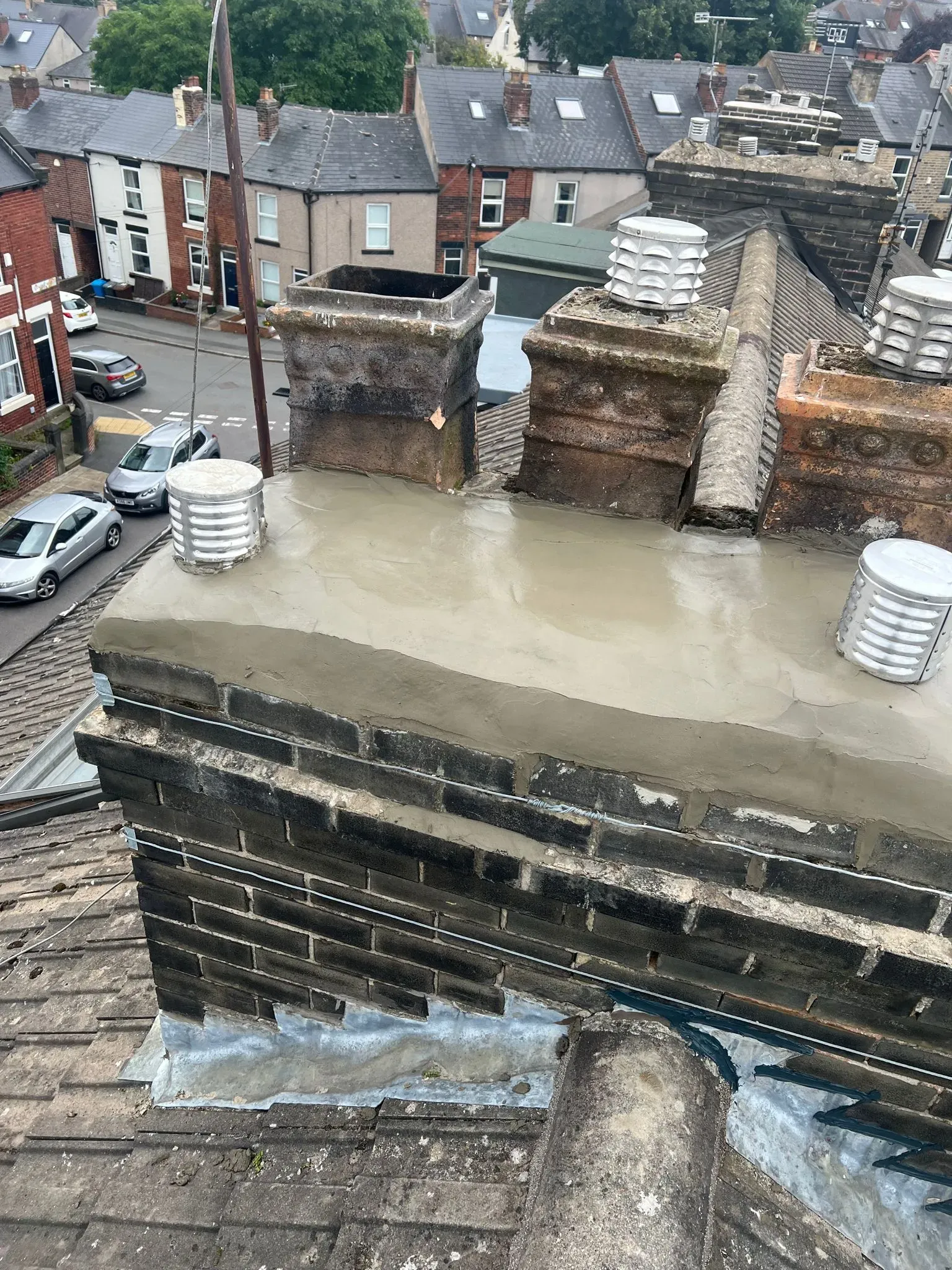 Recently repaired chimney stack on a house roof in Sheffield by Alliance Roofing Services, showing new cement work.