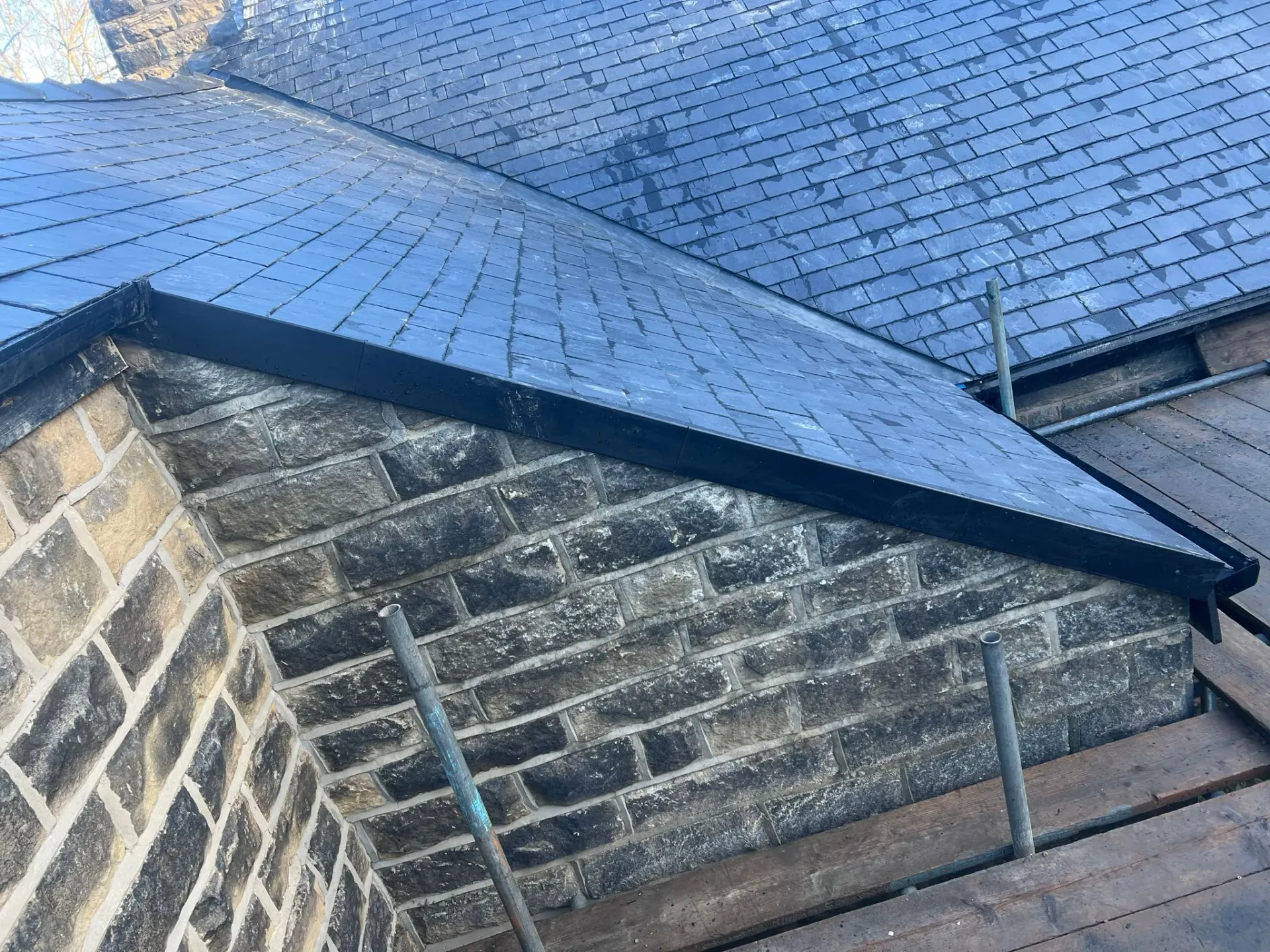 Slate roof installation or repair project showing roof tiles, stone wall, and scaffolding by Alliance Roofing Services in Sheffield or the Peak District.