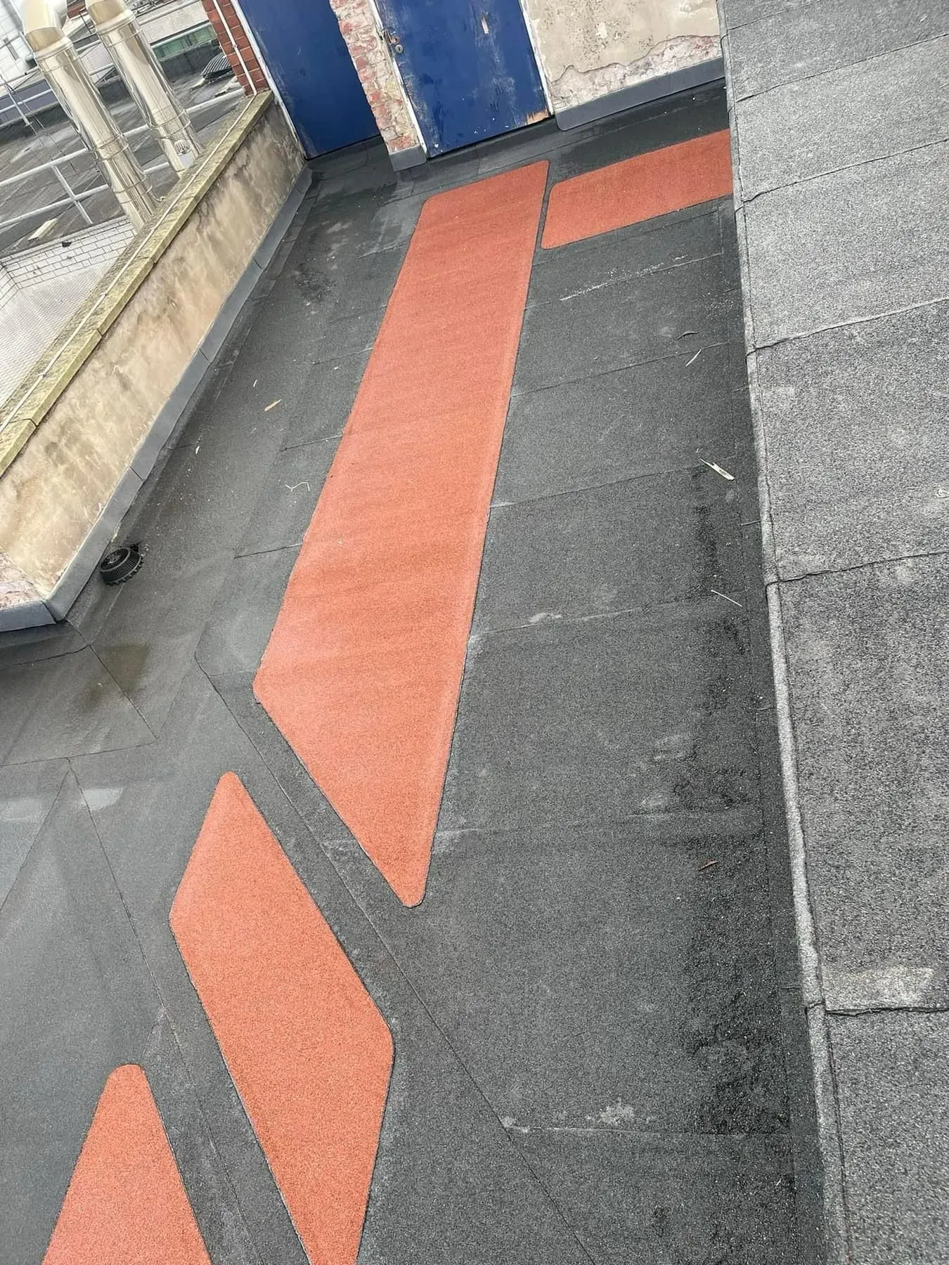 Close up of a flat roof surface with red aggregate design elements, a drain, and a parapet wall.
