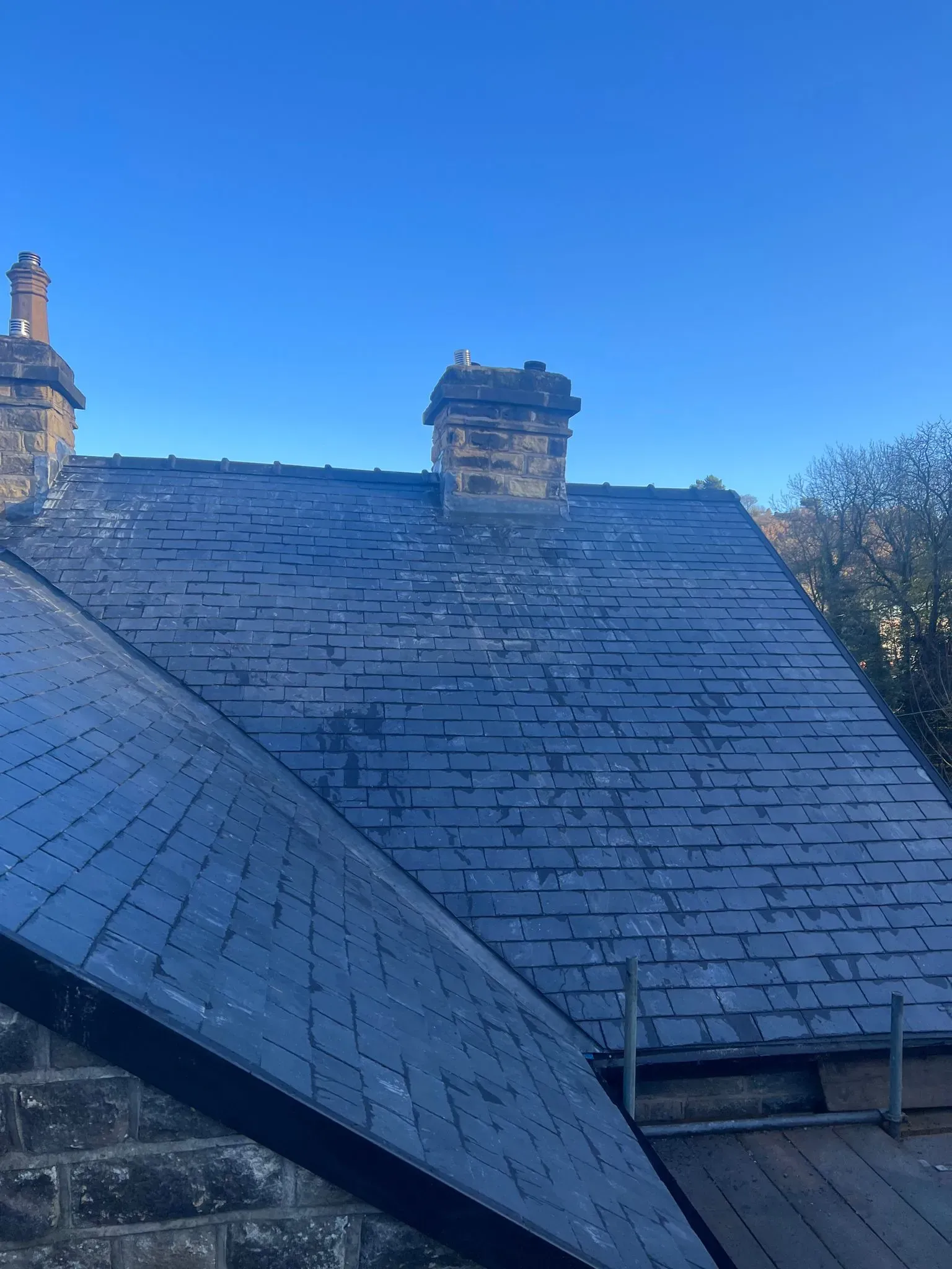Slate pitched roof with chimneys and scaffolding under blue sky.