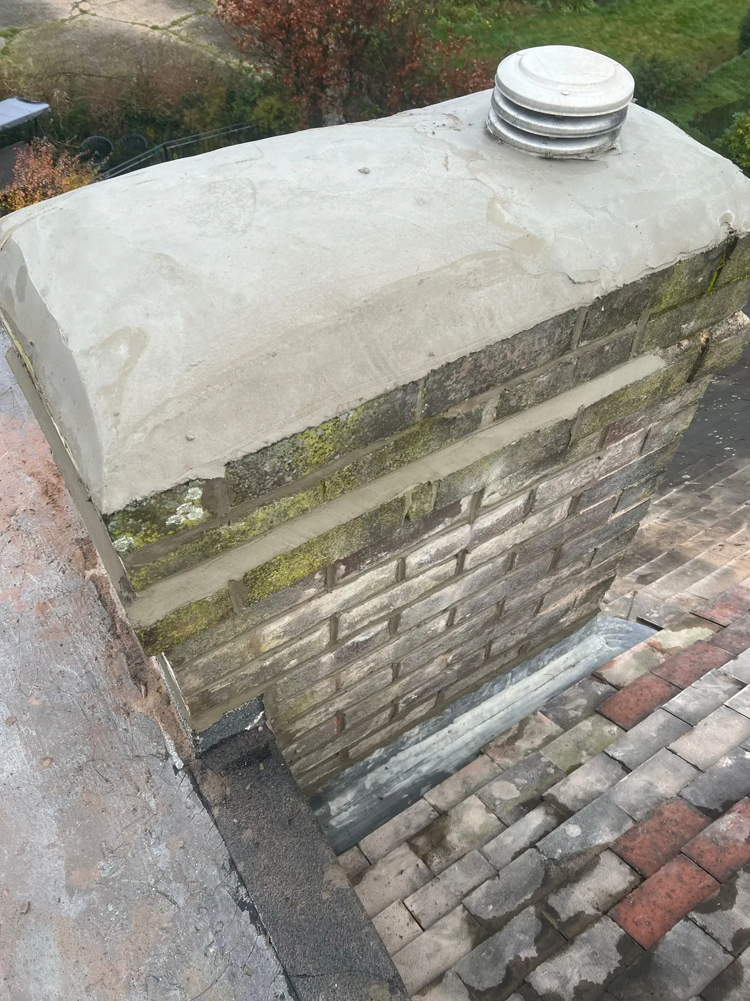 Close-up of a brick chimney on a pitched roof with a vent and recent mortar work.