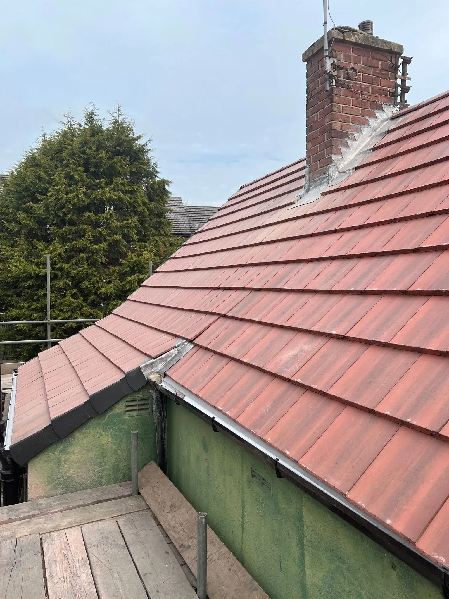 Pitched roof with red tiles, chimney, and lead flashing under repair or installation.