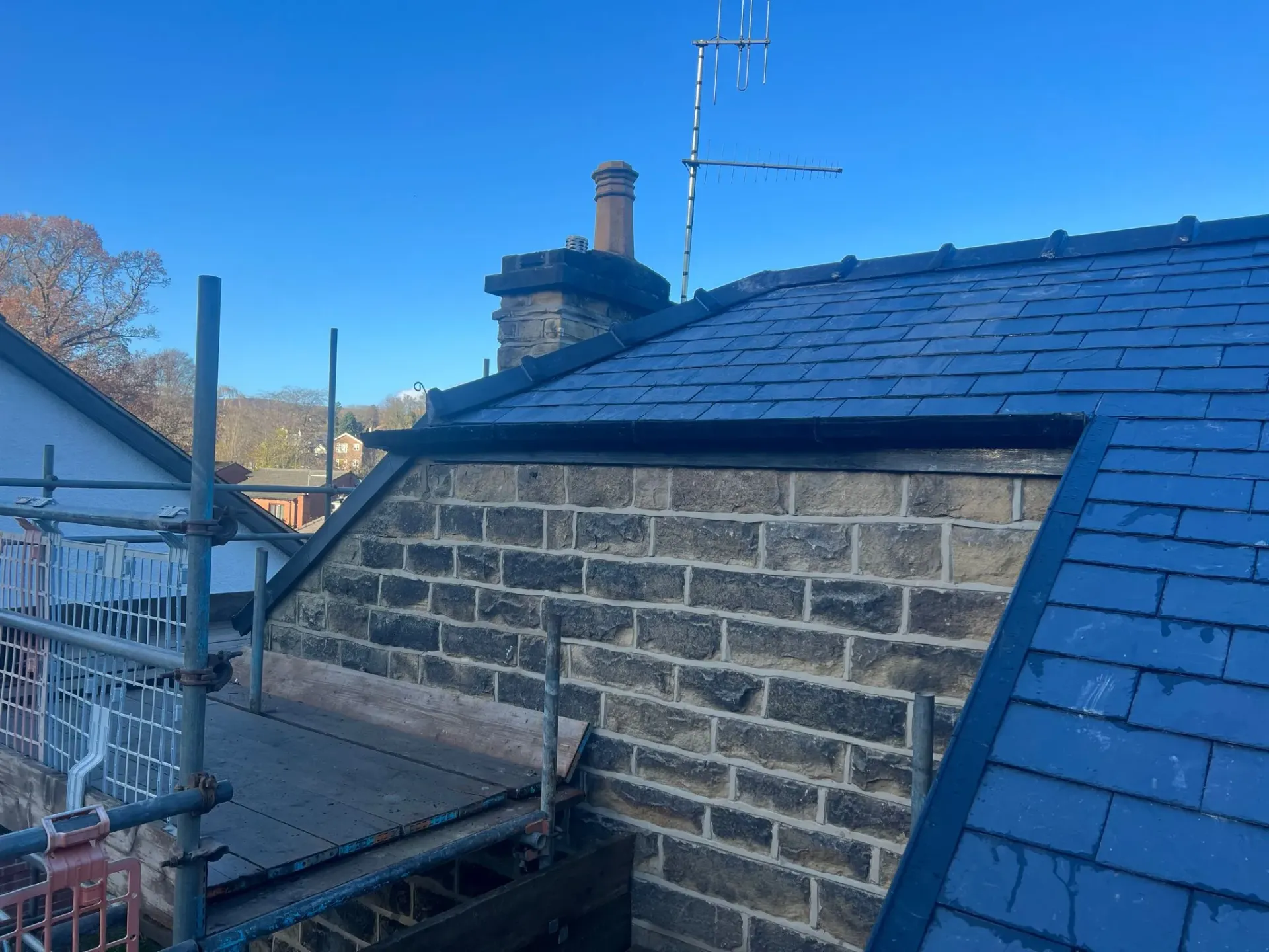 Pitched roof with slate tiles, stone wall, and scaffolding during roofing work in Sheffield or the Peak District