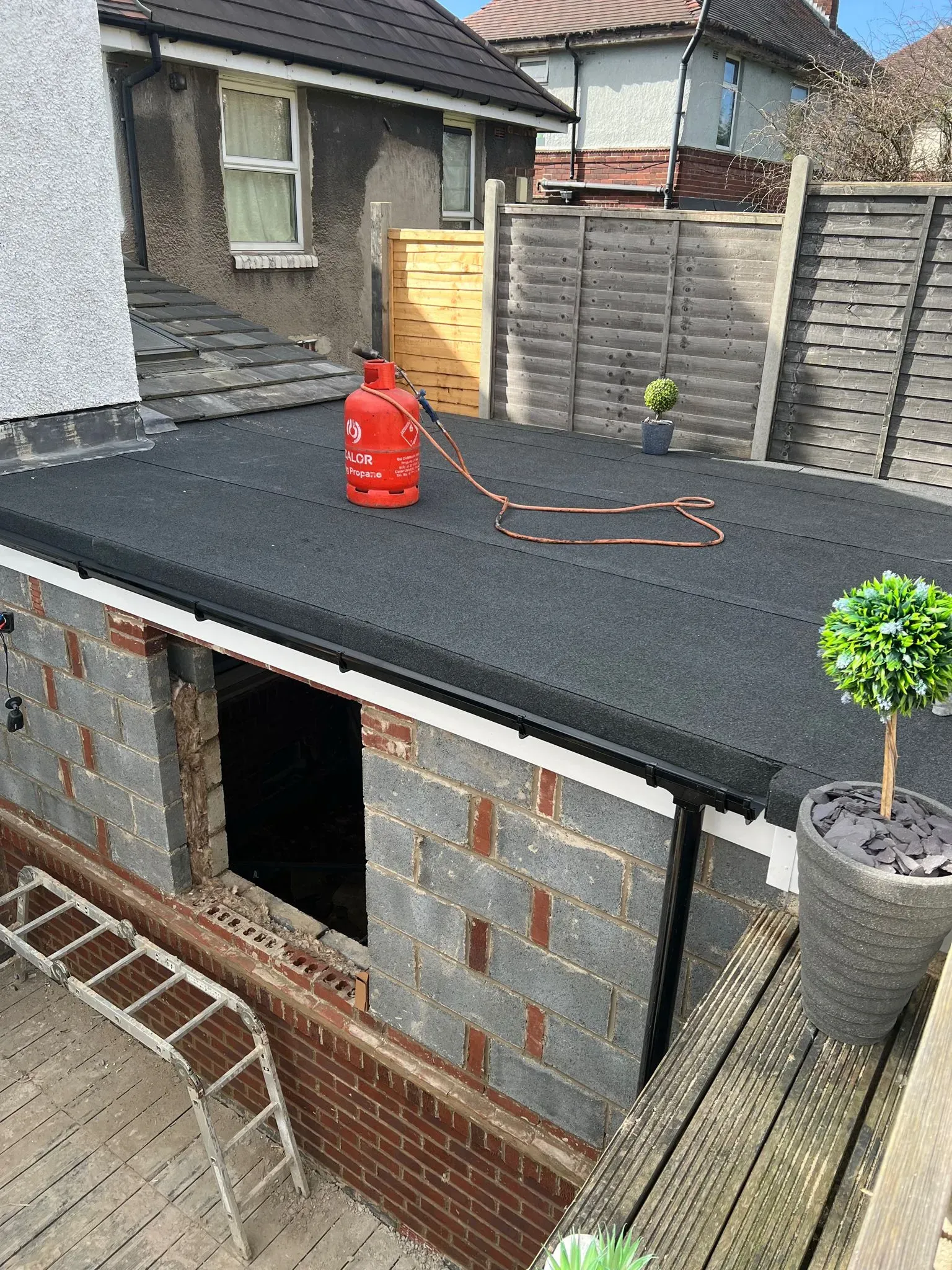 Newly installed flat roof on a residential extension with guttering and gas bottle